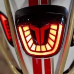 Close-up van de achterzijde van een scooter met rood LED-achterlicht, rode striping en blauw kenteken.