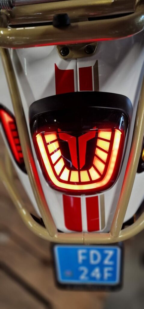 Close-up van de achterzijde van een scooter met rood LED-achterlicht, rode striping en blauw kenteken.