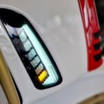 Detail van wit voertuig met verticale ledlamp, rode accentstrip en gouden spaakwiel.