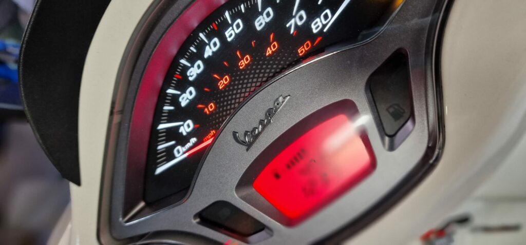 Close-up van een Vespa-scooter dashboard met snelheidsmeter en rood digitaal display.