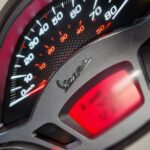 Close-up van een Vespa-scooter dashboard met snelheidsmeter en rood digitaal display.