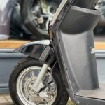 Close-up van het voorwiel en spatbord van een zwarte scooter, voor een winkelruit.