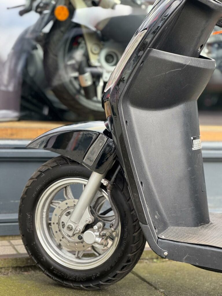 Close-up van het voorwiel en spatbord van een zwarte scooter, voor een winkelruit.