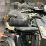 Close-up van een zwarte elektrische scootmobiel met lederen stoel, armleuningen en stuur.