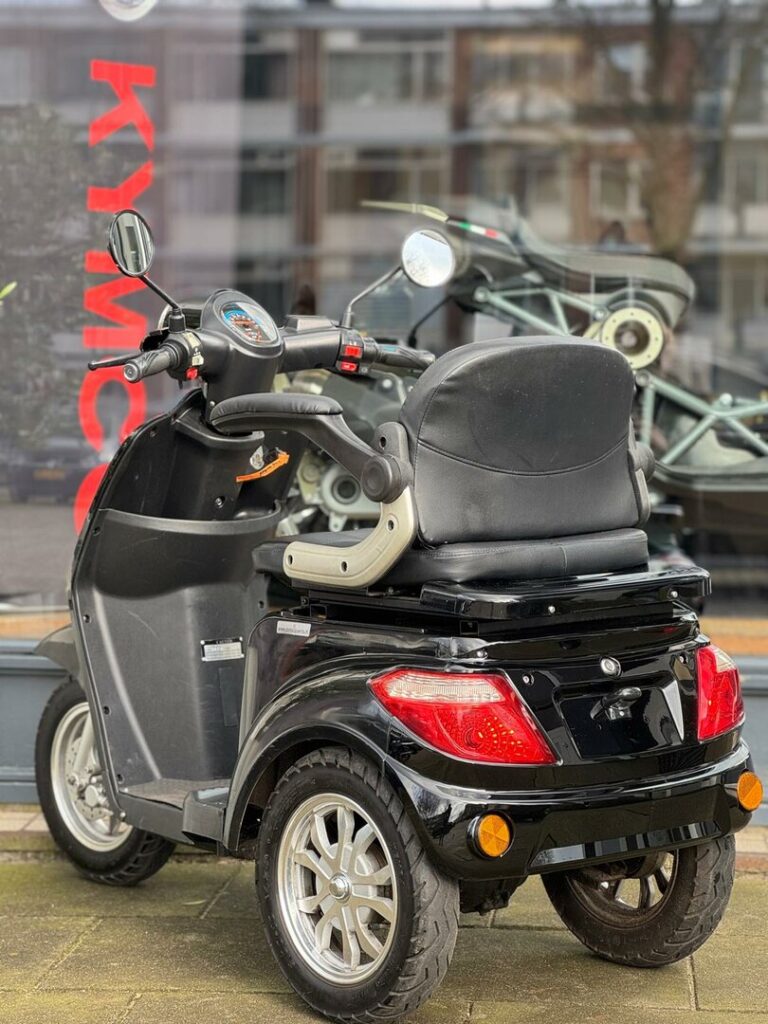 Zwarte driewielige scootmobiel geparkeerd voor een winkelraam met KYMCO-logo.