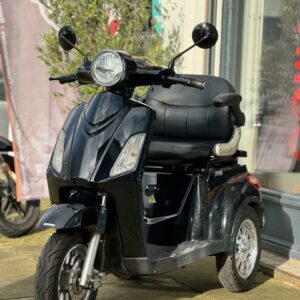 Zwarte driewielscooter geparkeerd voor een winkel, met grote koplamp en spiegels.