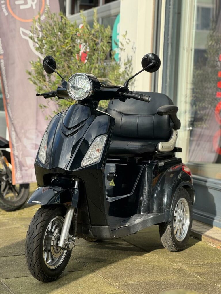 Zwarte driewielscooter geparkeerd voor een winkel, met grote koplamp en spiegels.