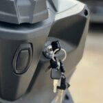 Close-up van een scooterstuur met sleutelbos in het contactslot, grijze kunststof afwerking.