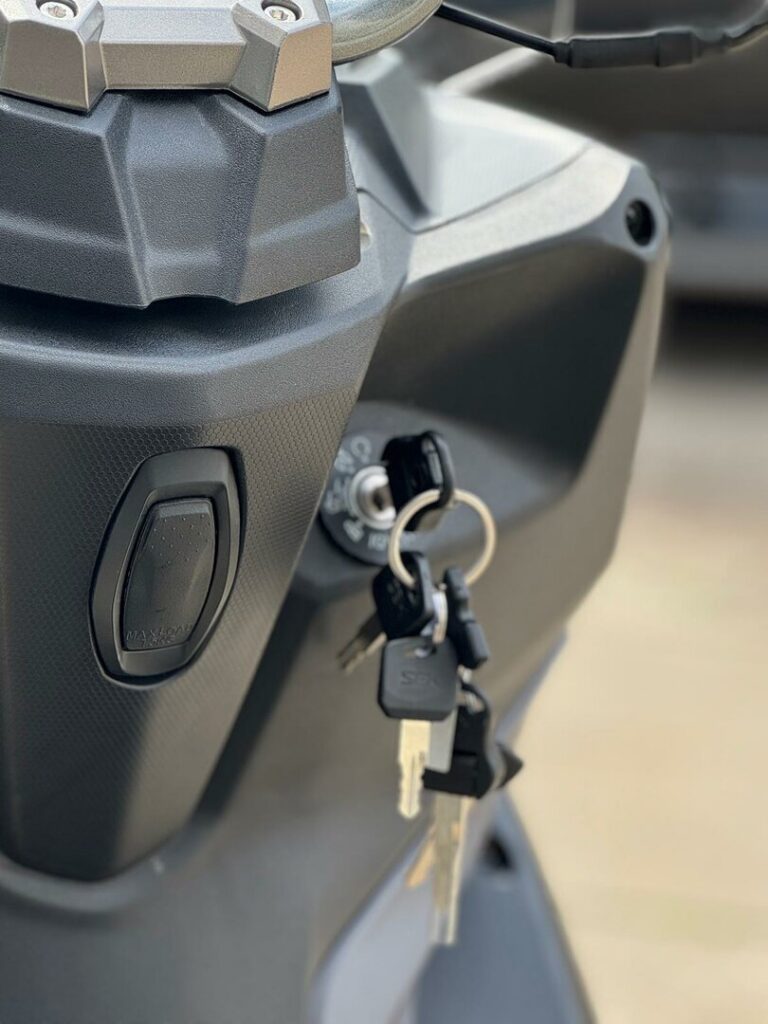 Close-up van een scooterstuur met sleutelbos in het contactslot, grijze kunststof afwerking.