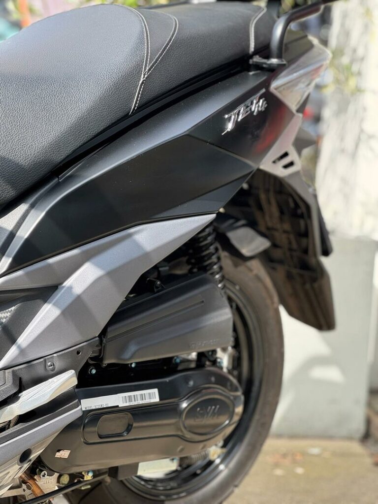 Close-up van de zijkant van een zwarte scooter met zadel, motorafdekking, achterwiel en vering.