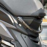 Close-up van een scooterzadel en zijkuip, met een opgerold gepantserd kabelslot.