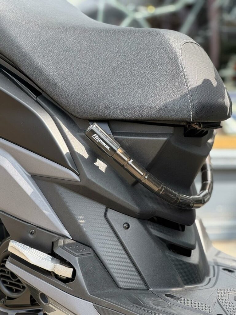 Close-up van een scooterzadel en zijkuip, met een opgerold gepantserd kabelslot.