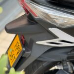 Close-up van de achterkant van een scooter met achterlicht, band en gele kentekenplaat.