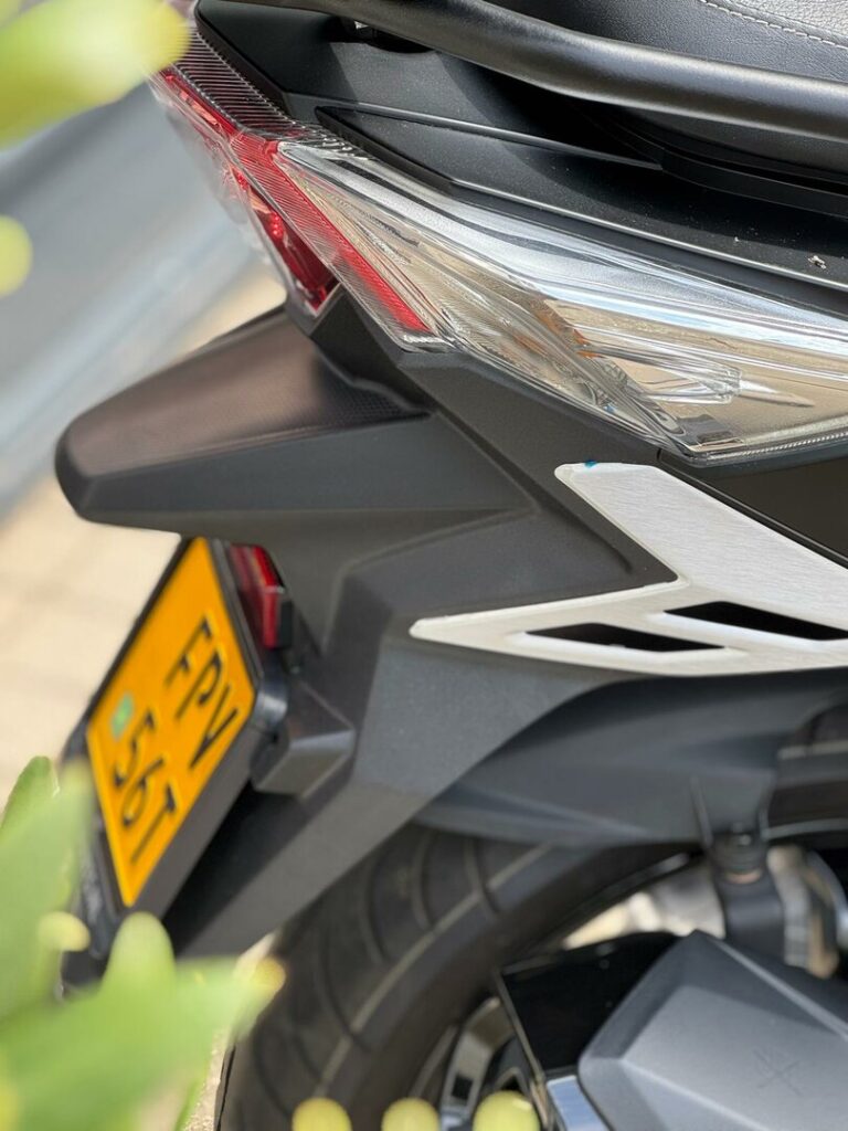 Close-up van de achterkant van een scooter met achterlicht, band en gele kentekenplaat.