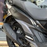 Close-up van de achterzijde van een zwarte scooter met uitlaat, wiel en grijs zadel.