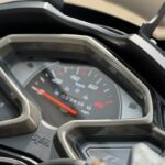 Close-up van het dashboard van een SYM-scooter met analoge snelheidsmeter en kilometerteller.