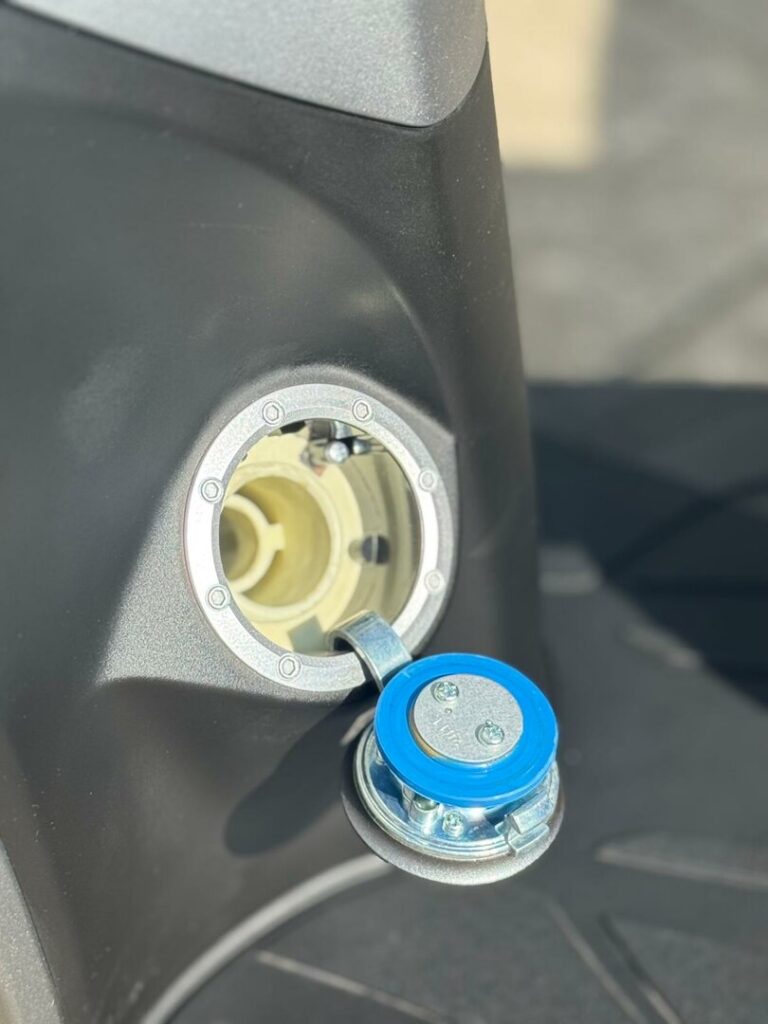 Open brandstofdop van een scooter, met blauwe dop op scharnier, close-up