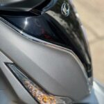 Close-up van de voorkant van een grijze scooter met richtingaanwijzer en koplampdetails.