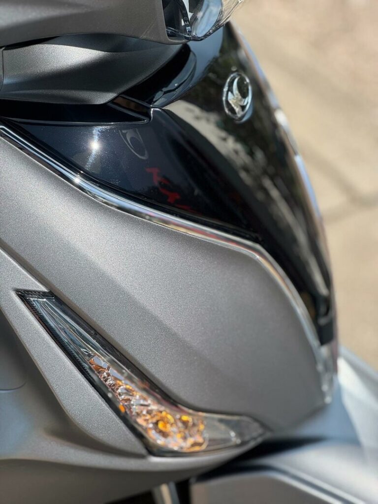 Close-up van de voorkant van een grijze scooter met richtingaanwijzer en koplampdetails.