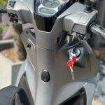 Close-up van stuur en digitaal dashboard van een grijze scooter met rode sleutels