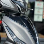 Close-up van de voorzijde van een zilveren KYMCO-scooter met scherpe LED-koplampen.