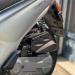 Close-up van de achterzijde van een zilveren scooter met vering, wiel en motorblok.