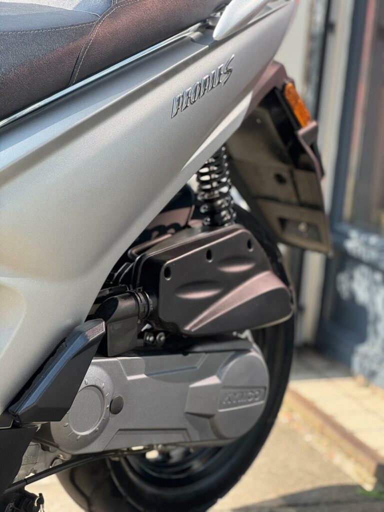 Close-up van de achterzijde van een zilveren scooter met vering, wiel en motorblok.