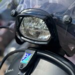 Close-up van de koplamp en het windscherm van een Vespa Sprint scooter met Piaggio-logo.