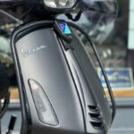 Close-up van de voorkant van een matte grijze Vespa-scooter met koplamp en ventilatieroosters.