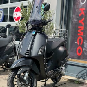 Matte zwarte scooter met hoog windscherm geparkeerd voor een scootershop.