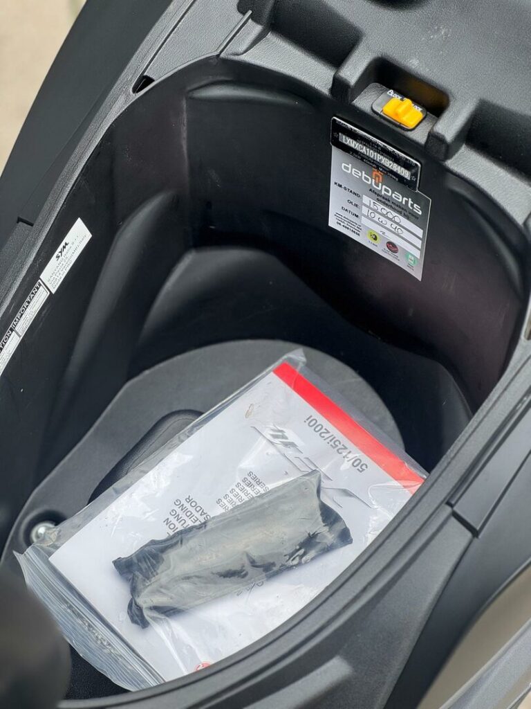 Opbergruimte onder het zadel van een scooter met handleiding en gereedschapsset.