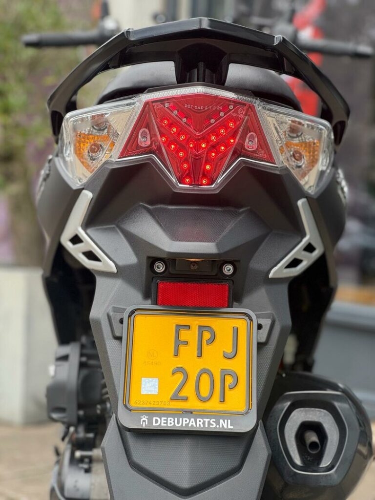 Achterkant van een scooter met brandend led-achterlicht en gele Nederlandse kentekenplaat.