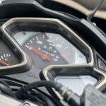 Close-up van het instrumentenpaneel van een SYM-motor, met snelheidsmeter en brandstofmeter.