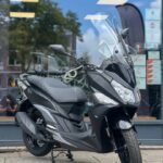 Zwarte scooter met hoog windscherm geparkeerd op de stoep voor een winkelraam.