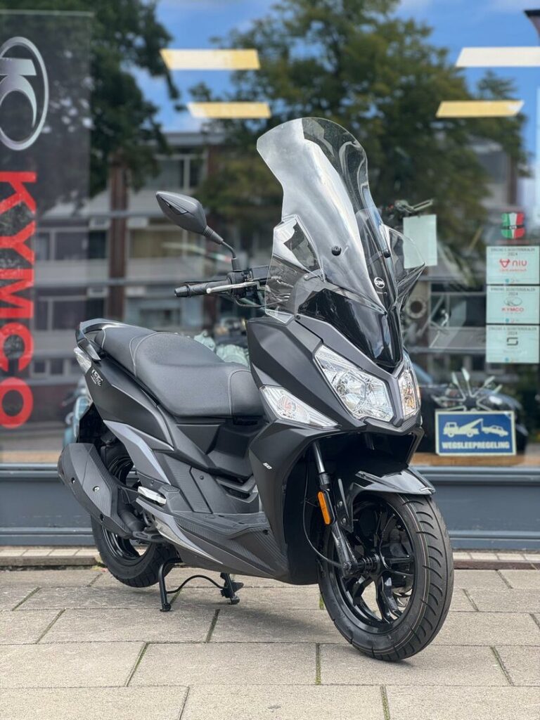 Zwarte motorscooter met hoog windscherm en LED-koplampen, geparkeerd voor showroom.