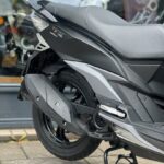 Detail van achterwiel, uitlaat en zadel van een matzwarte scooter op standaard.