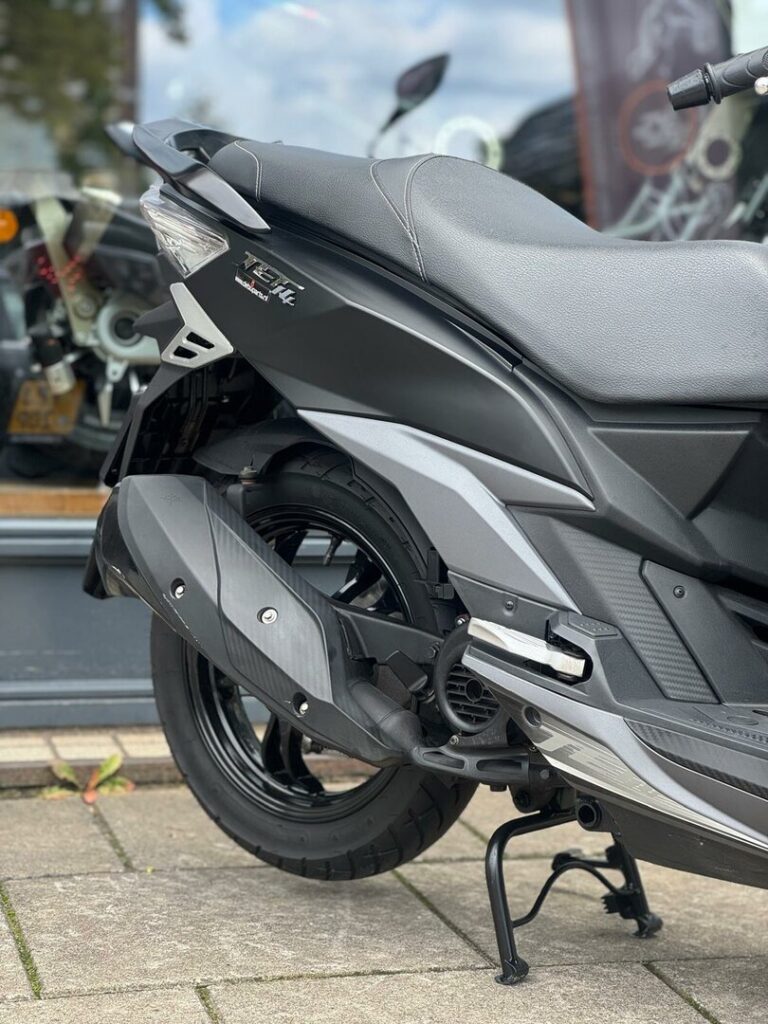 Detail van achterwiel, uitlaat en zadel van een matzwarte scooter op standaard.