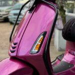 Close-up van de voorkant van een metallic roze scooter met oranje knipperlicht.