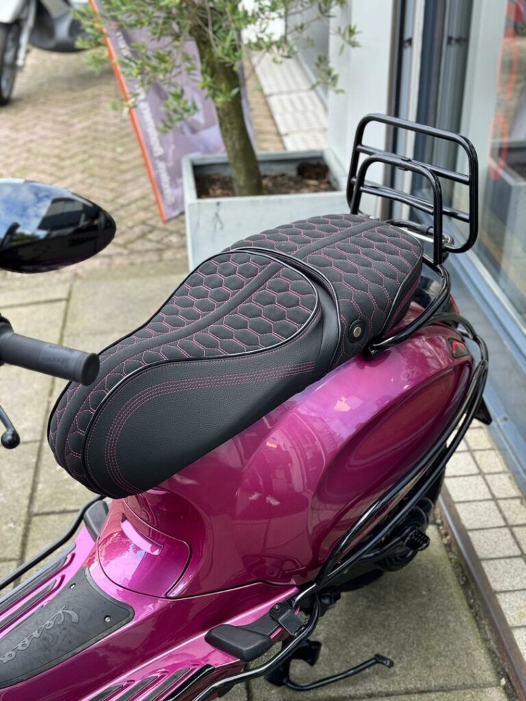 Detail van een magenta scooter met zwart zadel met honingraatstiksel en achterdrager.