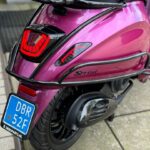 Achterzijde van een magenta Vespa Sprint scooter met LED-achterlicht en blauw NL-kenteken.