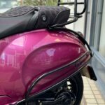 Close-up van de achterzijde van een paarse Vespa-scooter met zwart zadel en bagagedrager.