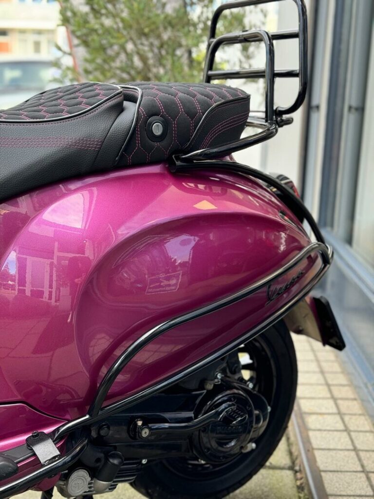 Close-up van de achterzijde van een paarse Vespa-scooter met zwart zadel en bagagedrager.