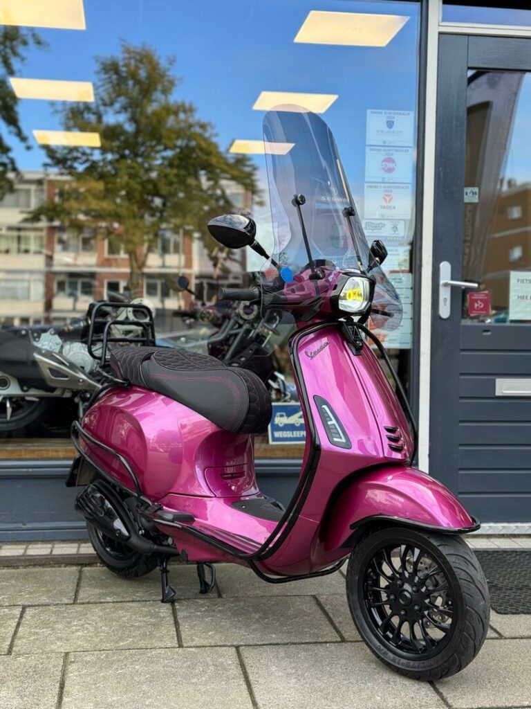Fuchsia Vespa-scooter met hoog windscherm, geparkeerd voor een winkelpui.
