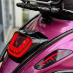 Close-up van de achterzijde van een paarse scooter met rode LED-achterlichten en bagagedrager.