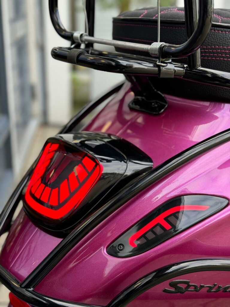 Close-up van de achterzijde van een paarse scooter met rode LED-achterlichten en bagagedrager.