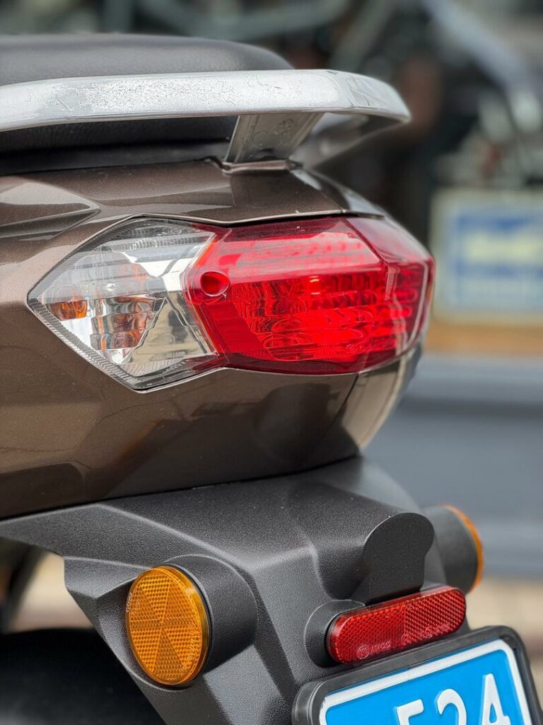 Achterkant van scooter met rood achterlicht, knipperlichten en bagagedrager.