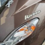 Close-up van de voorkant van een bruine Peugeot Kisbee-scooter met brandend knipperlicht.