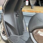 Voetplaat en middenkolom van een Peugeot Kisbee scooter met contactsleutel en label.