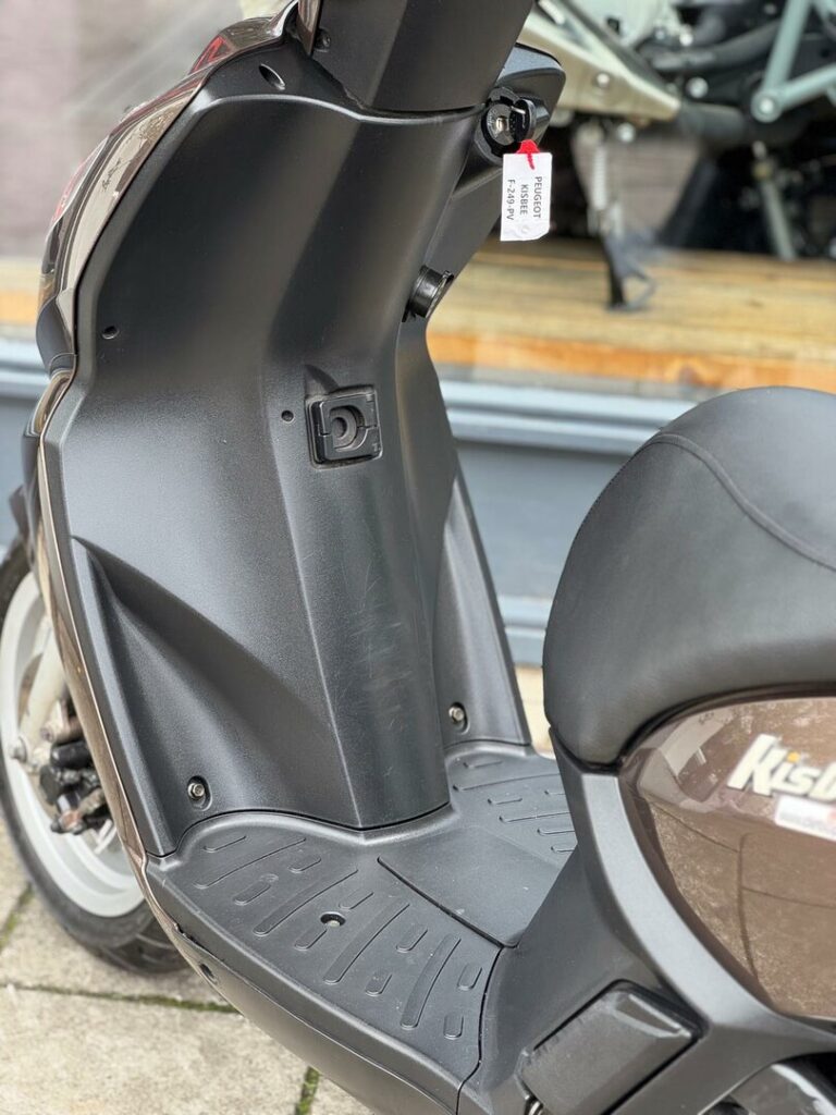 Voetplaat en middenkolom van een Peugeot Kisbee scooter met contactsleutel en label.