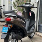 Bruine scooter vanaf achterzijde op standaard, geparkeerd voor een winkel.